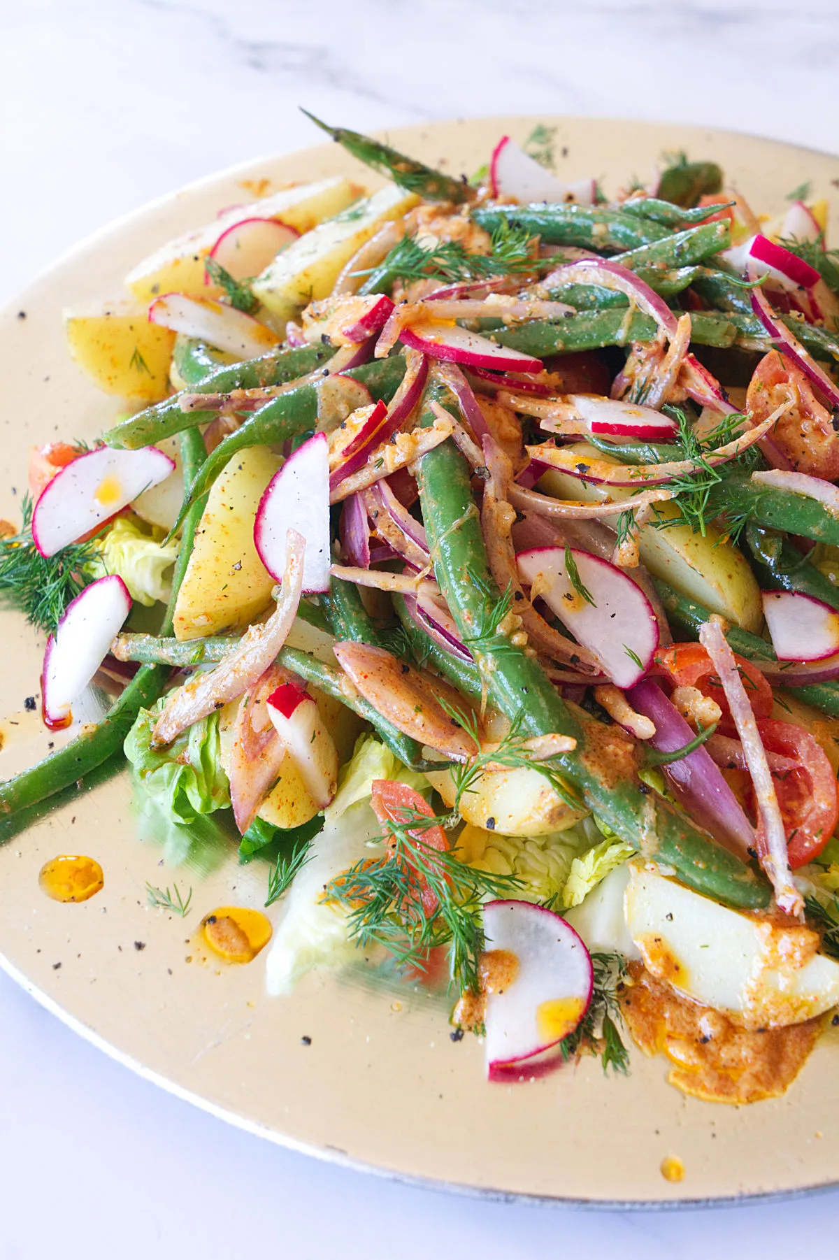 A platter of no-mayo potato salad is garnished with red onion and green beans.