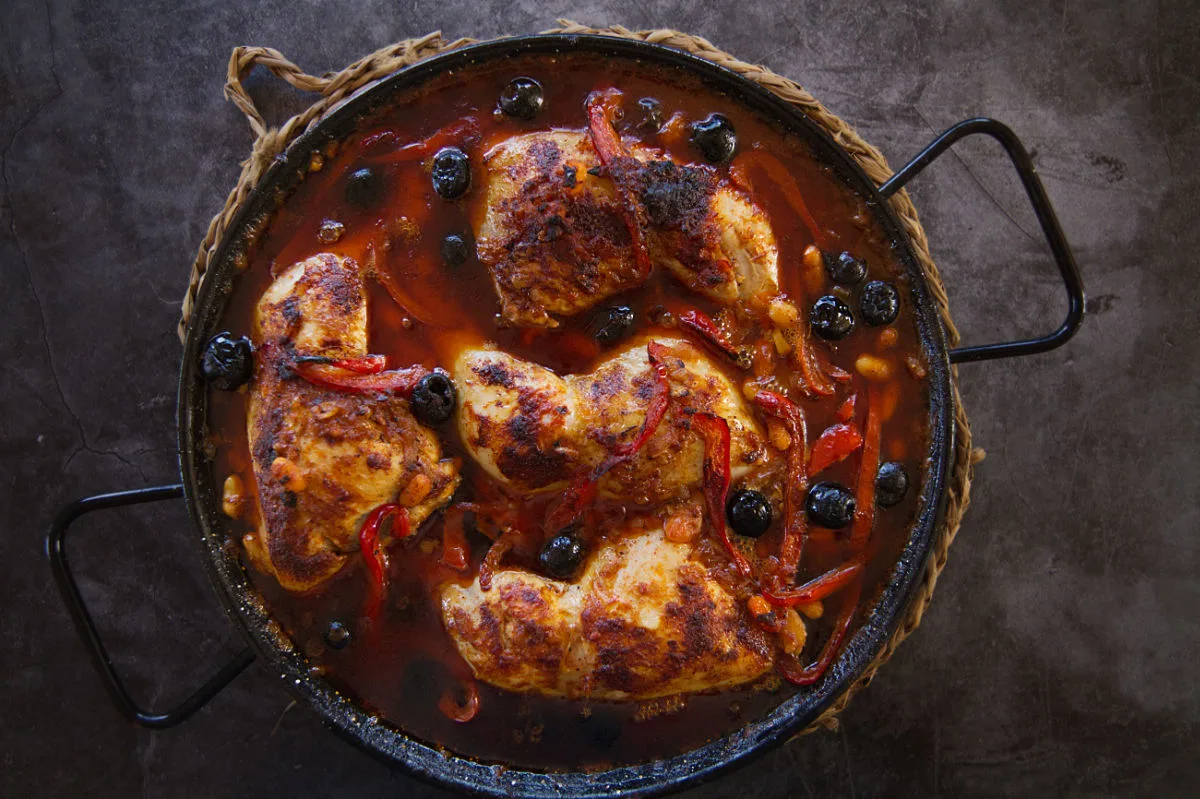 A pan of Spanish chicken with smoky Bravas sauce sits at a table setting.