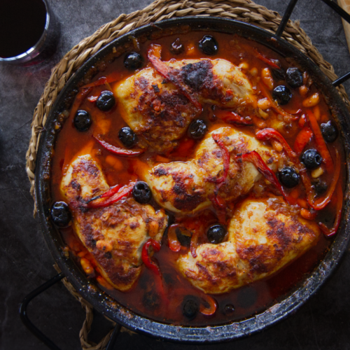 A pan of Spanish chicken with smoky Bravas sauce sits at a table setting.