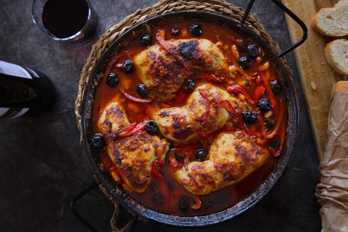 A pan of Spanish chicken with smoky Bravas sauce sits at a table setting.