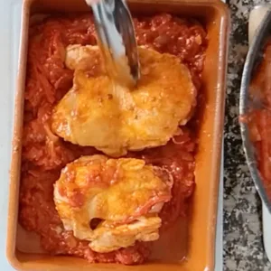 Browned chicken pieces in a dish with sofrito sauce.