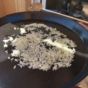 Diced onion cooks in a large paella pan with some oil