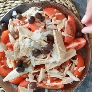 Sliced onion an black olives are sprinnkled on top of a tuna tomato salad.