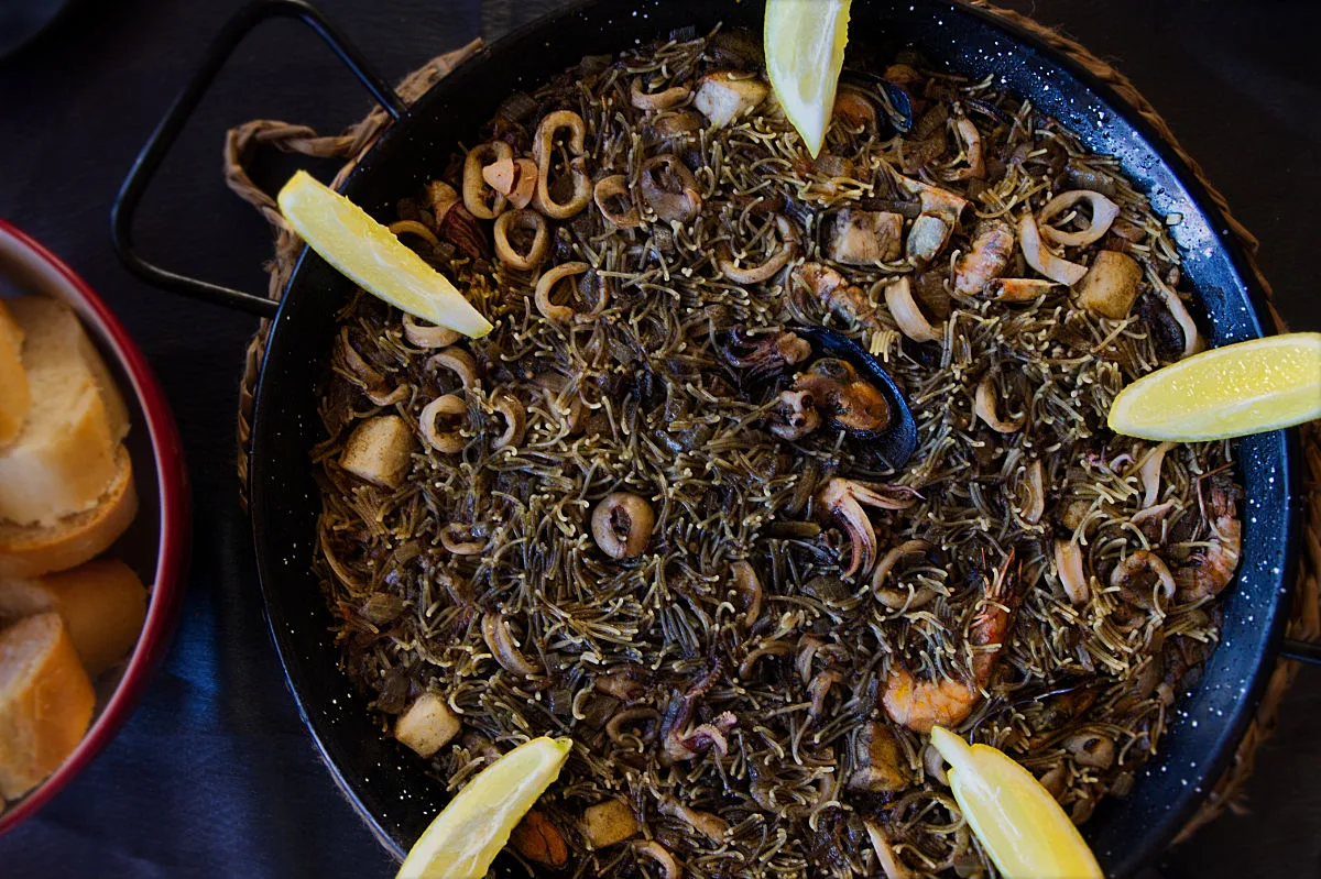 Fideua negra with seafood in a large pan.