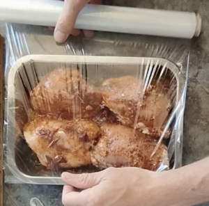 Chicken thighs in a tray are wrapped in plastic kitchen foil.