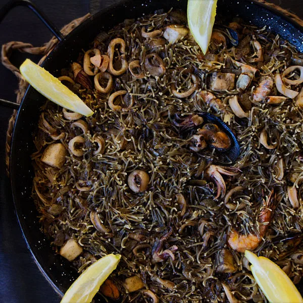 Fideua negra with seafood in a large pan.