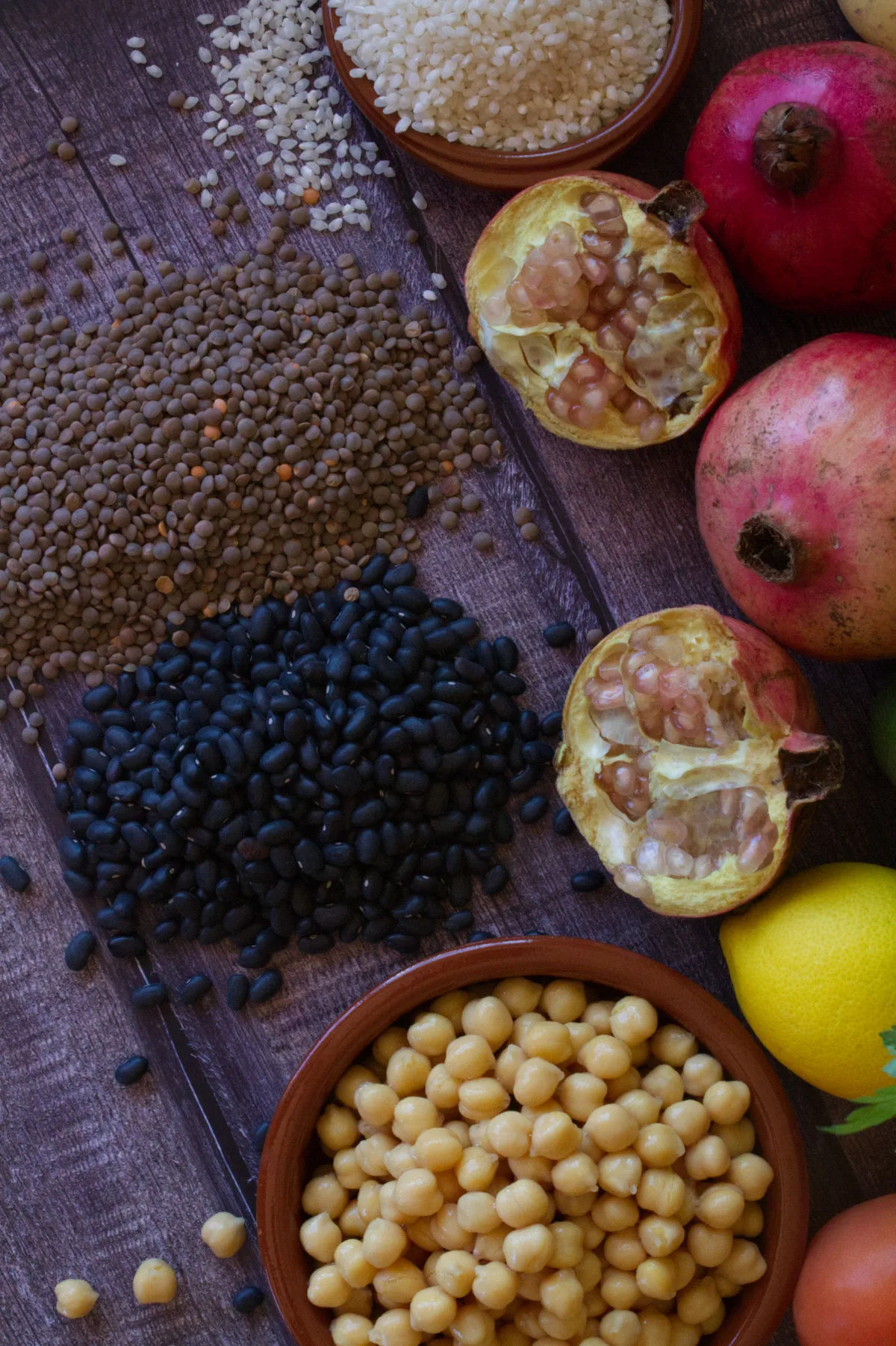 legumes, seeds, rice, ad pasta are arranged beside some pomegranates, lemons, and chickpeas.