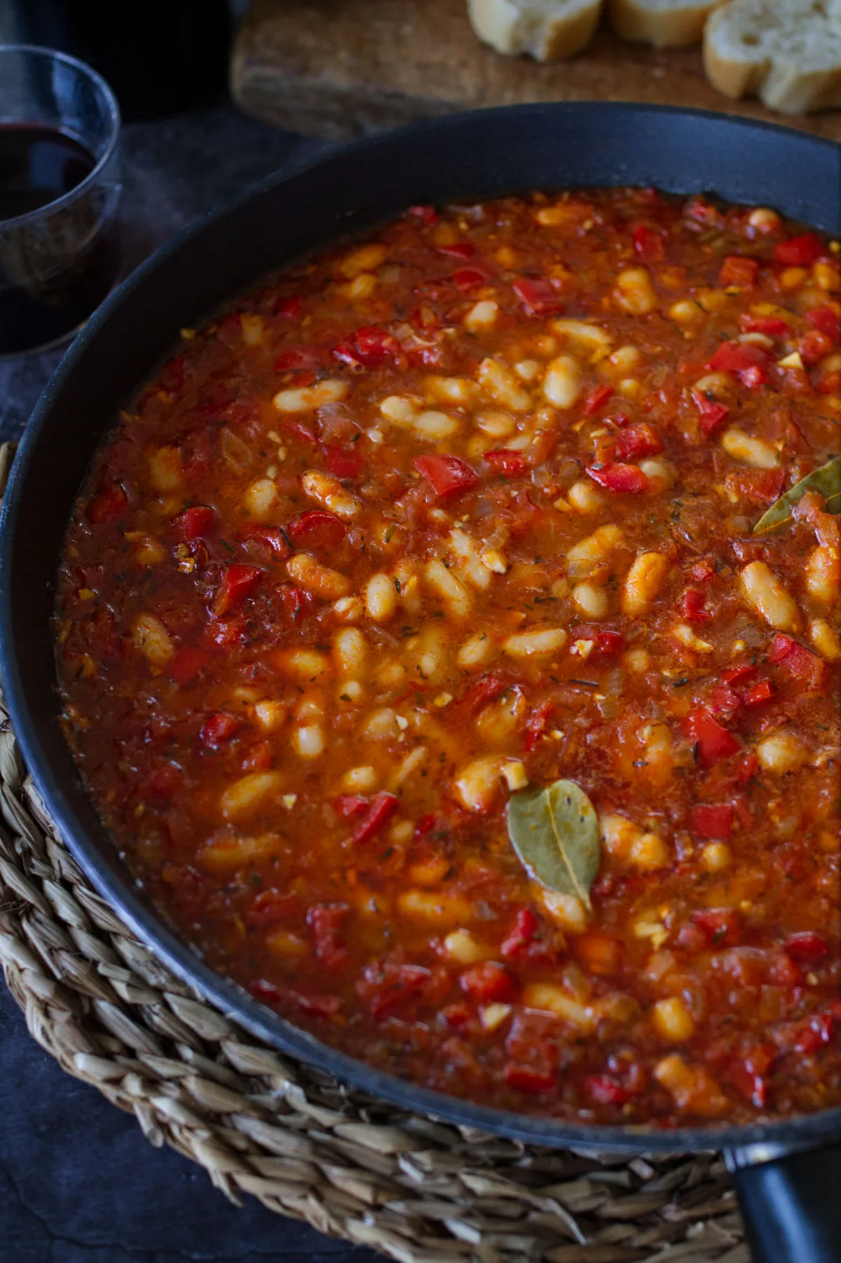 a large pan of white bean stew sits with a few bay leaves on top.