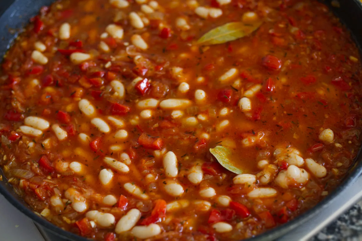 A large pan of Spanish-style white bean stew simmers on a stovetop