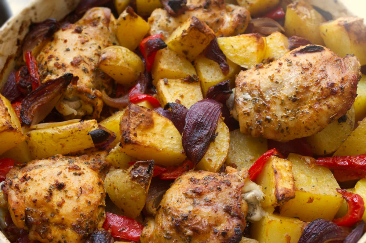 A large dish of cooked chicken thighs and roasted potatoes.