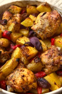 A large dish of cooked chicken thighs and roasted potatoes.