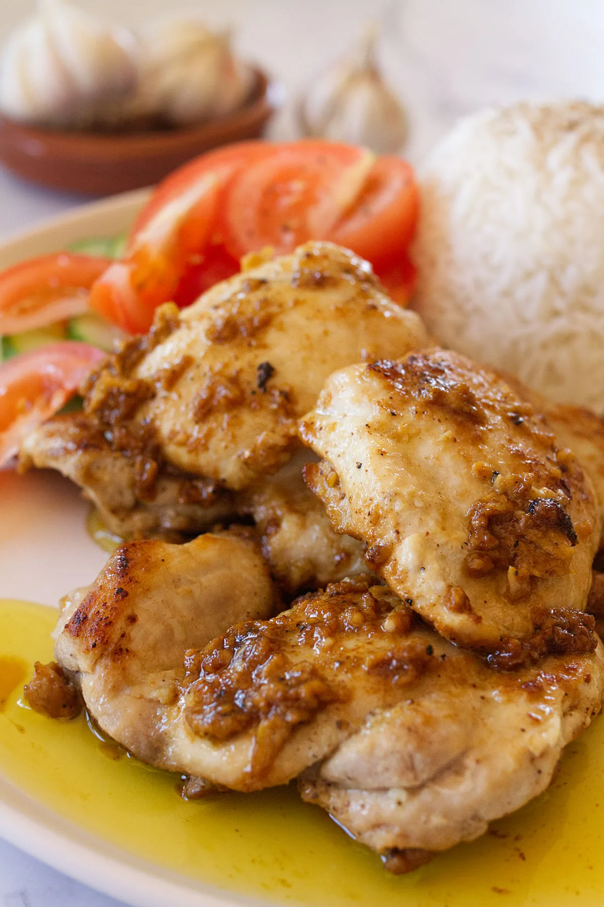 garlic-infused chicken thighs sit on a plate beside some steamed rice and salad. 