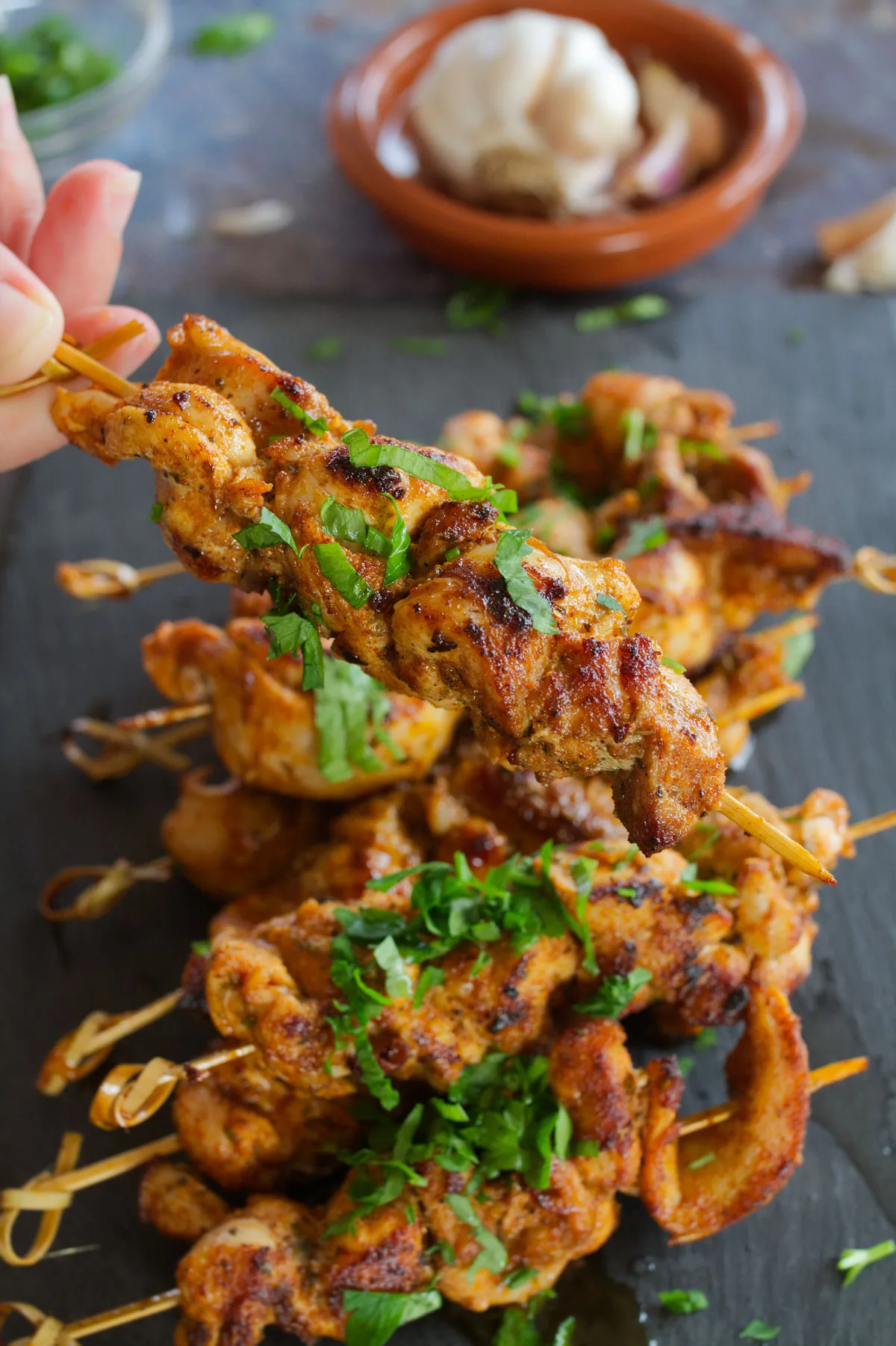 A small pile of paprika-infused chicken skewers sit on a slate plate.