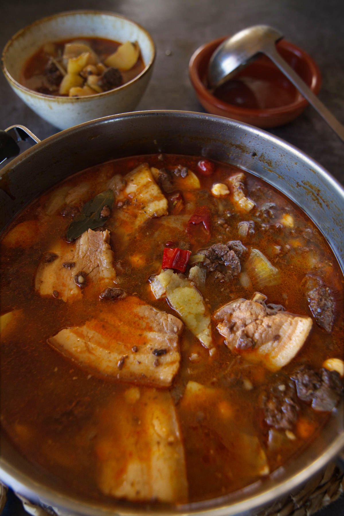 A large pot of spicy Spanish-style pork stew is served to a small bowl.