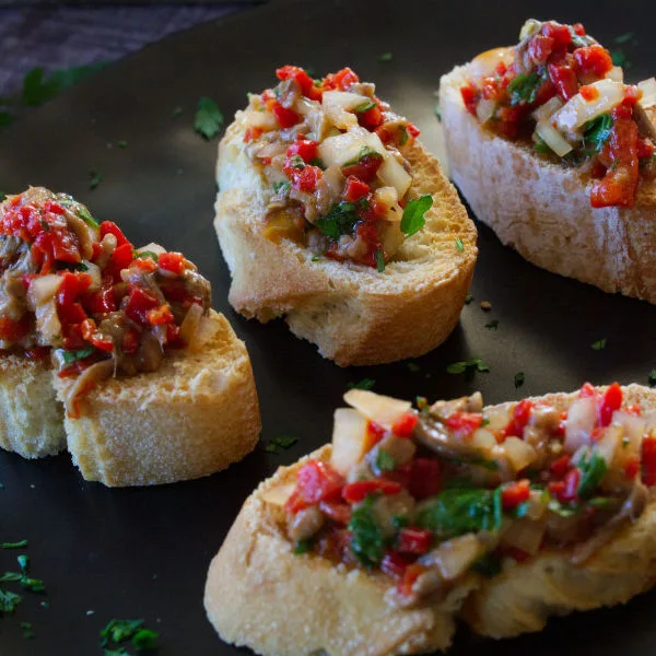 A small bowl of anchovy and pepper spread sists next to some served canapes.