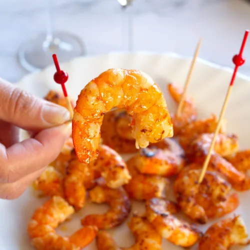 Some cooked shrimp on skewers sit beside two glasses of Cava.