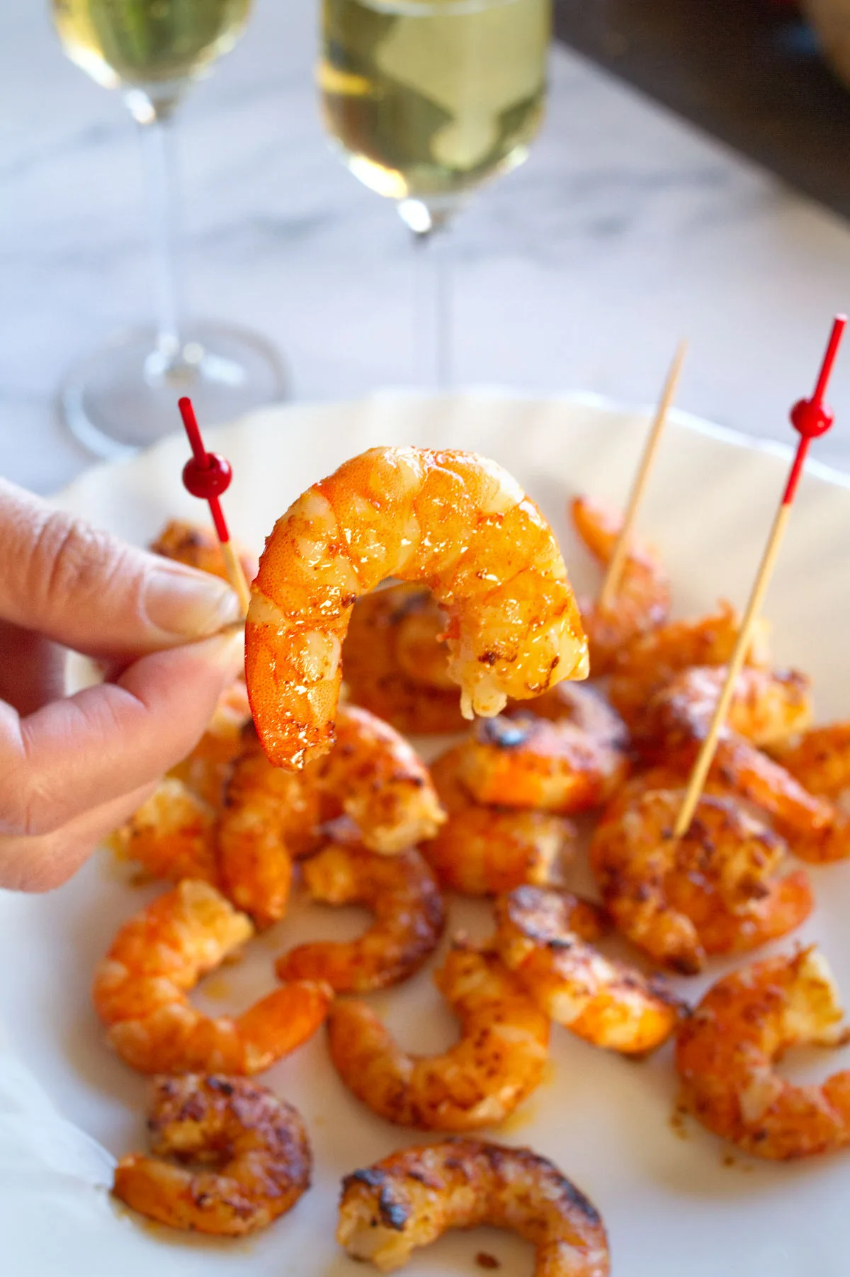 Some cooked shrimp on skewers sit beside two glasses of Cava.