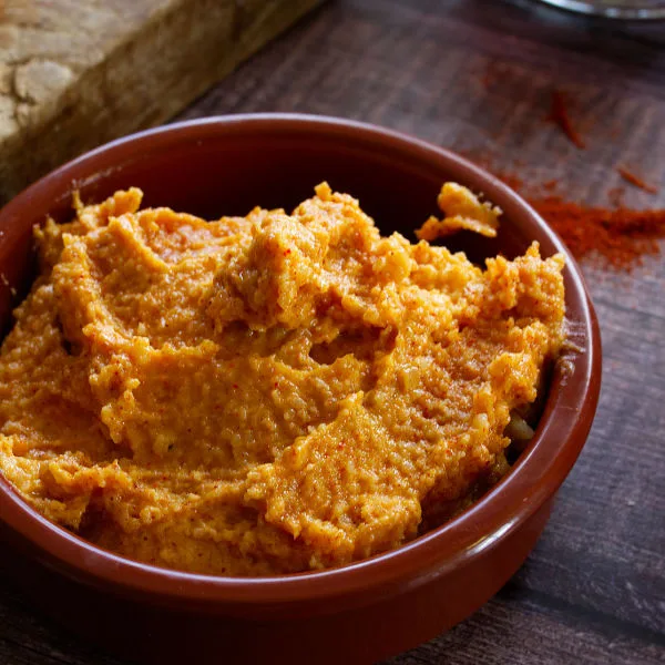 A bowl of Almogrote spiced cheese dip sits beside some slices of bread and some red wine.