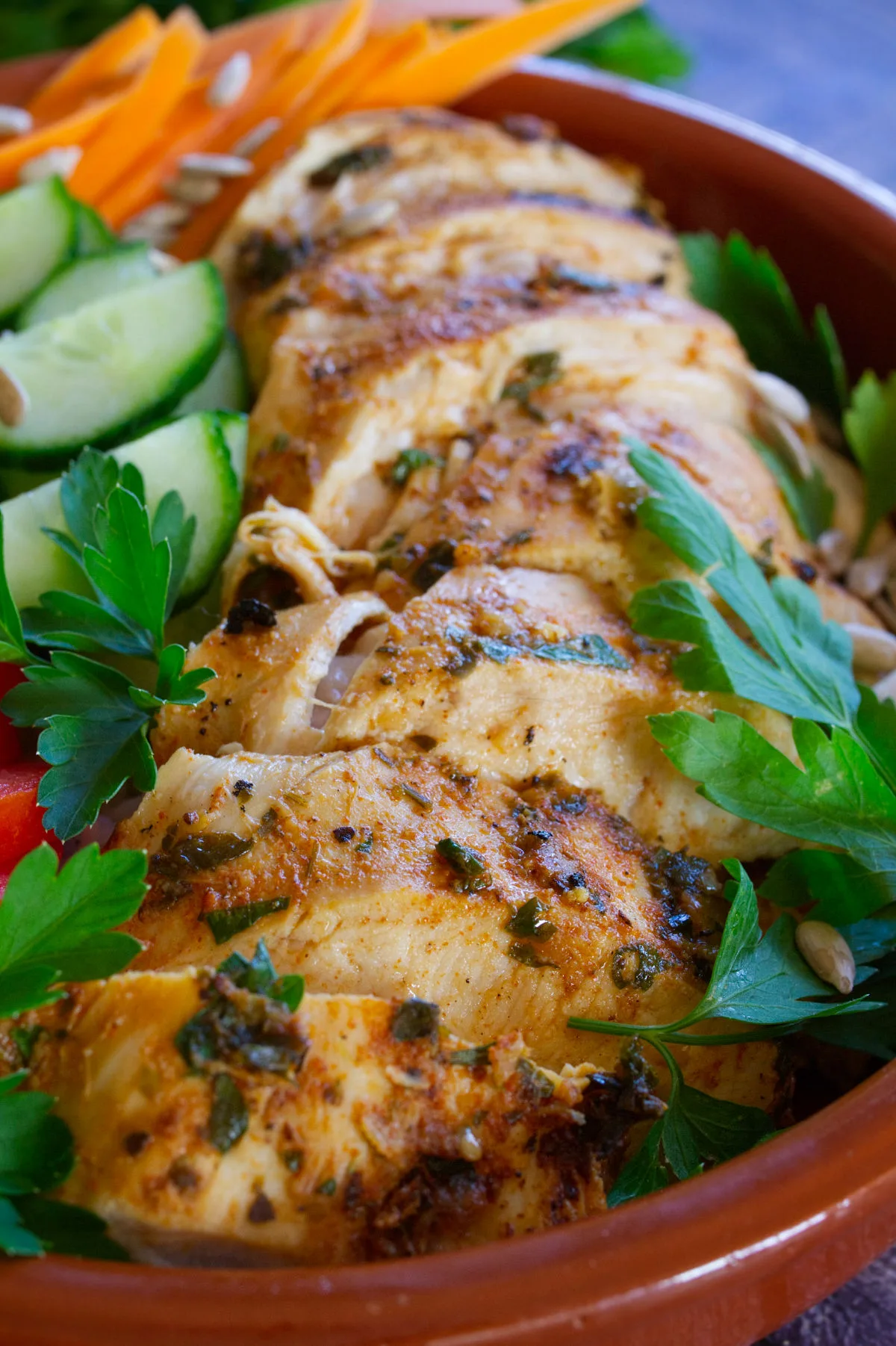 Slices of grilled Mediterranean chicken breast sit in a bowl with some salad.