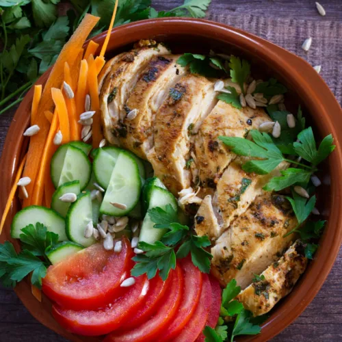 Slices of grilled Mediterranean chicken breast sit in a bowl with some salad.