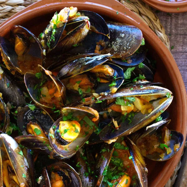 Spanish mussels in a rich tomato sofrito sauce sit in a bowl garnished with some fresh parsley.