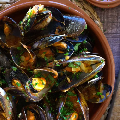 Spanish mussels in a rich tomato sofrito sauce sit in a bowl garnished with some fresh parsley.