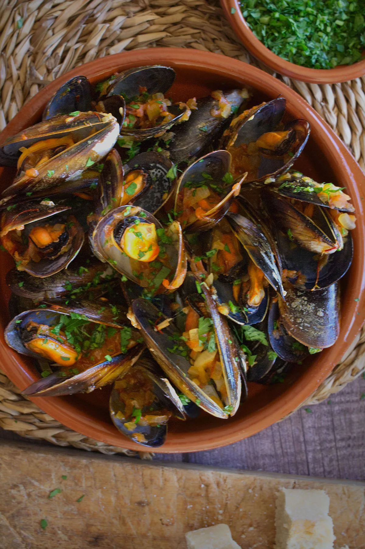 Spanish mussels in a rich tomato sofrito sauce sit in a bowl garnished with some fresh parsley.