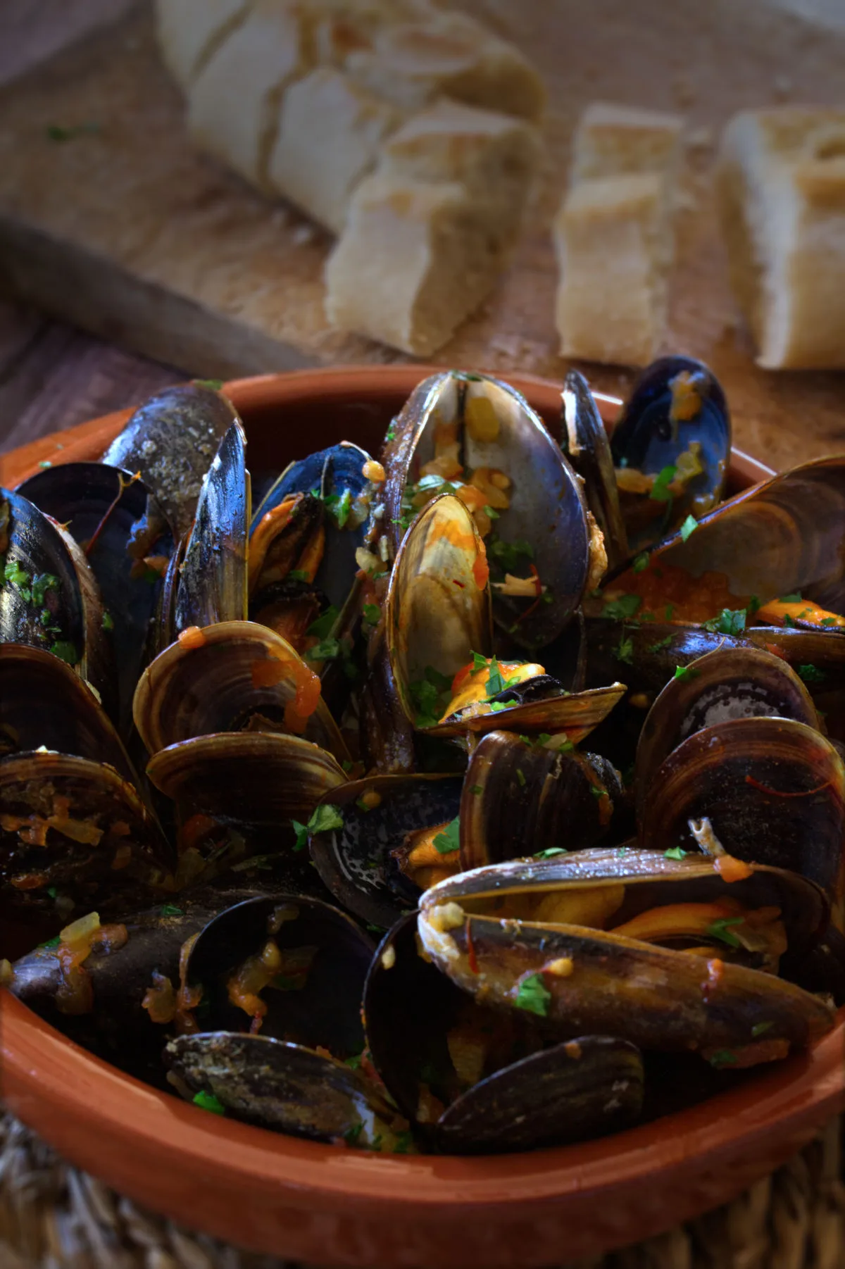 Spanish mussels in a rich tomato sofrito sauce sit in a bowl garnished with some fresh parsley.