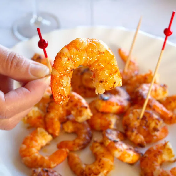 Some cooked shrimp on skewers sit beside two glasses of Cava.