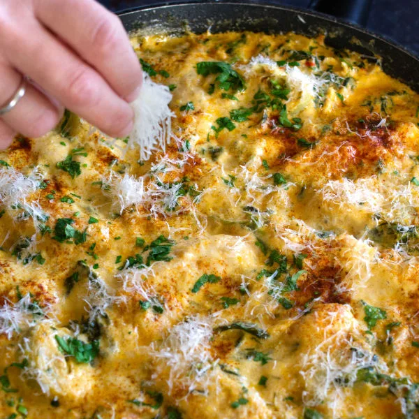 A large pan of cooked artichoke chicken sits garnished with grated parmesan cheese.