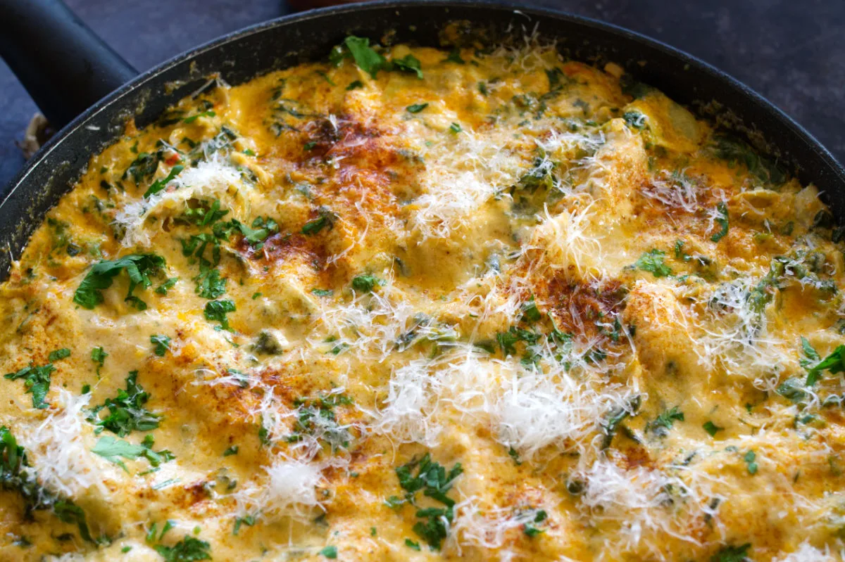 A large pan of creamy artichoke chicken with spinach and paprika.