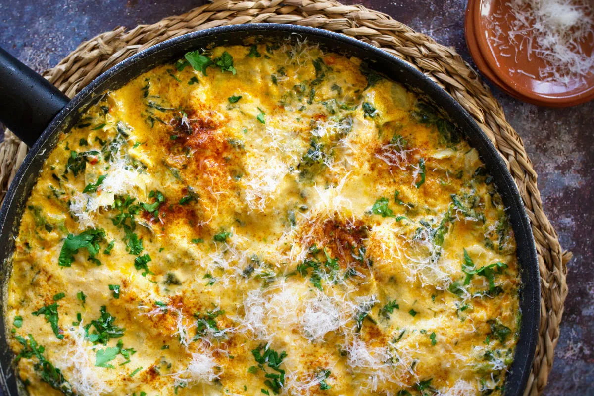 A large pan of creamy artichoke chicken with spinach and paprika.