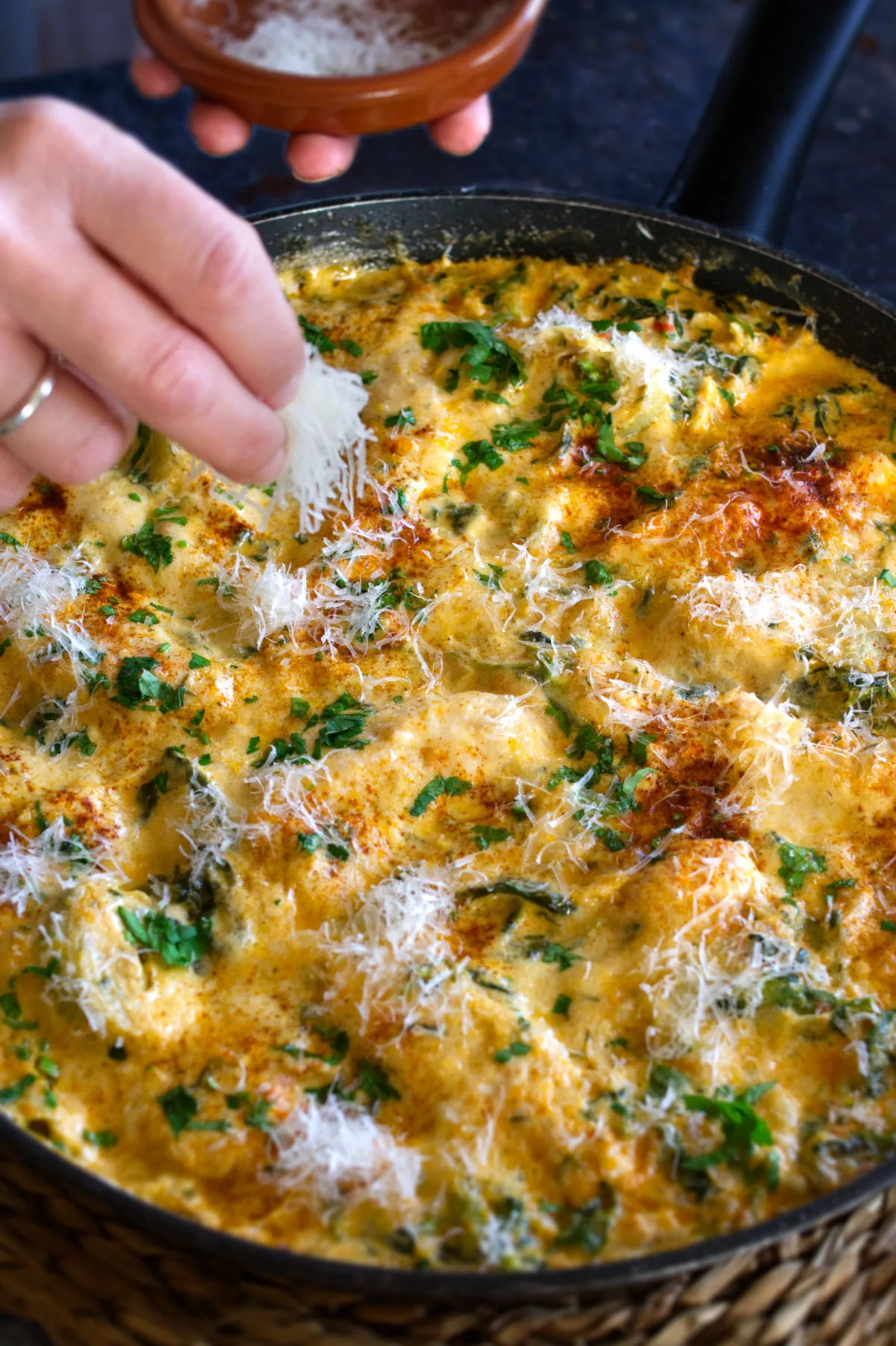 A large pan of cooked artichoke chicken sits garnished with grated parmesan cheese.