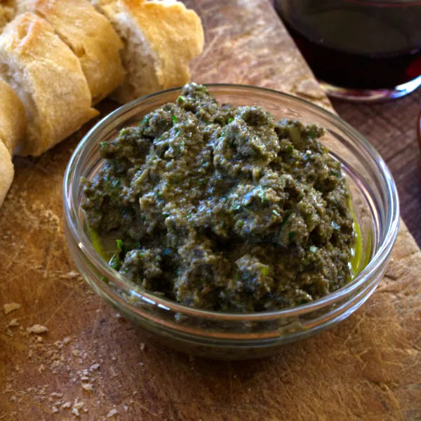 A small bowl of olive tapenade sits beside some sliced bread.