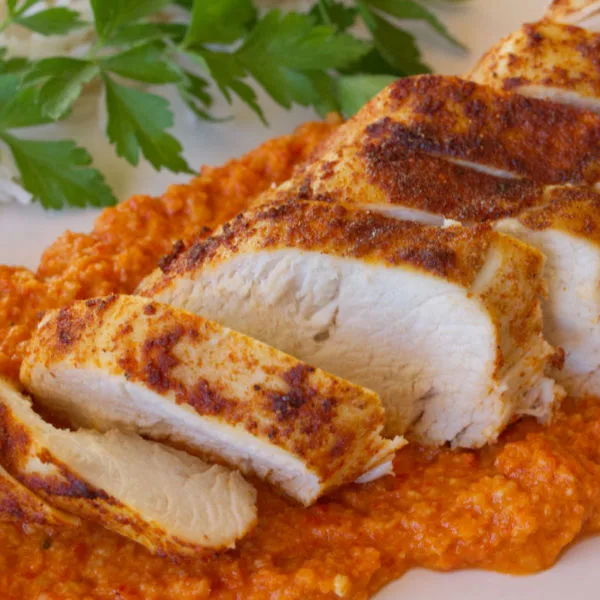 A plate fo sliced Roasted chicken breast with romesco sauce.