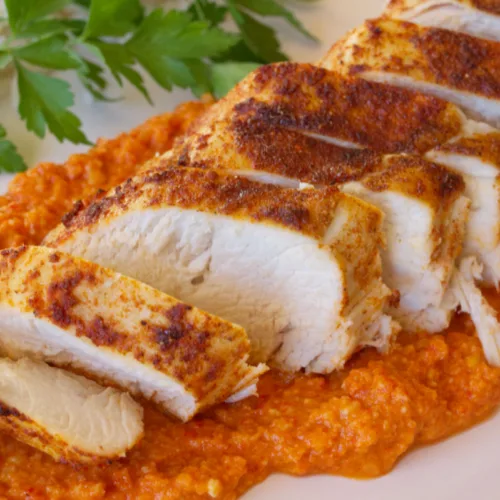 A plate fo sliced Roasted chicken breast with romesco sauce.