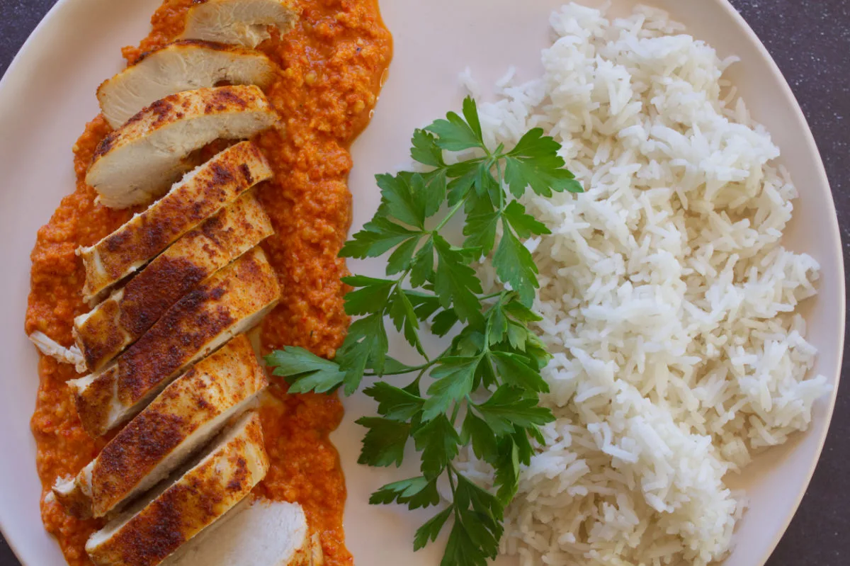 A plate fo sliced Roasted chicken breast with romesco sauce.