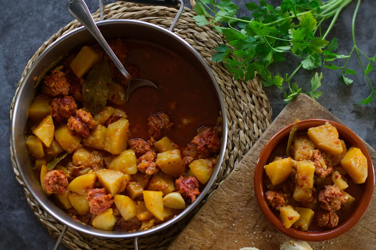 A large pot of Rioja-style potatoes with chorizo sits beside a small bowl serving.