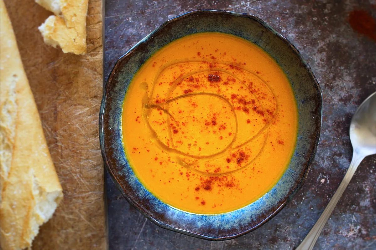 A bowl of carrot soup sits beside a large spoon.