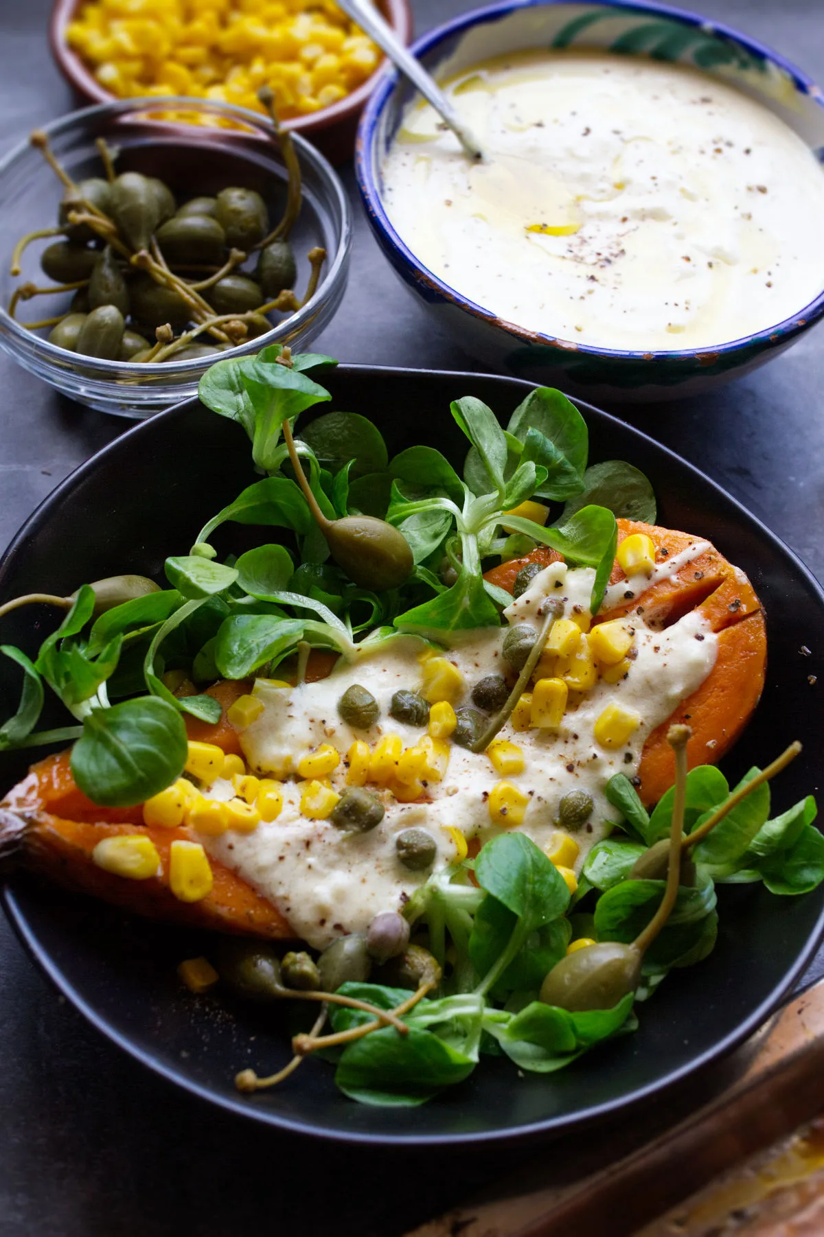 A baked sweet potato in a bowl with some salad and a dressing on top.