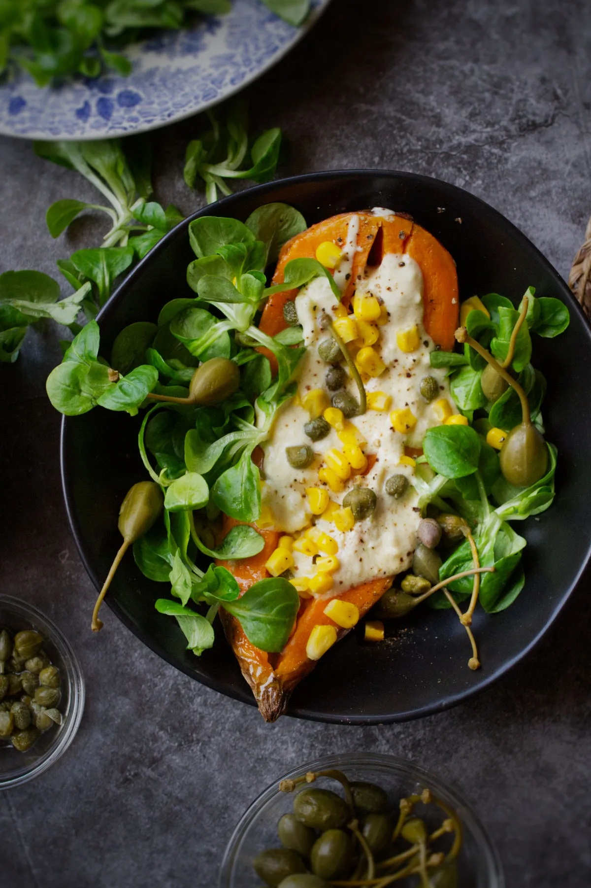 A bowl of baked sweet potato with toppings, salad, and a yogurt dressing.