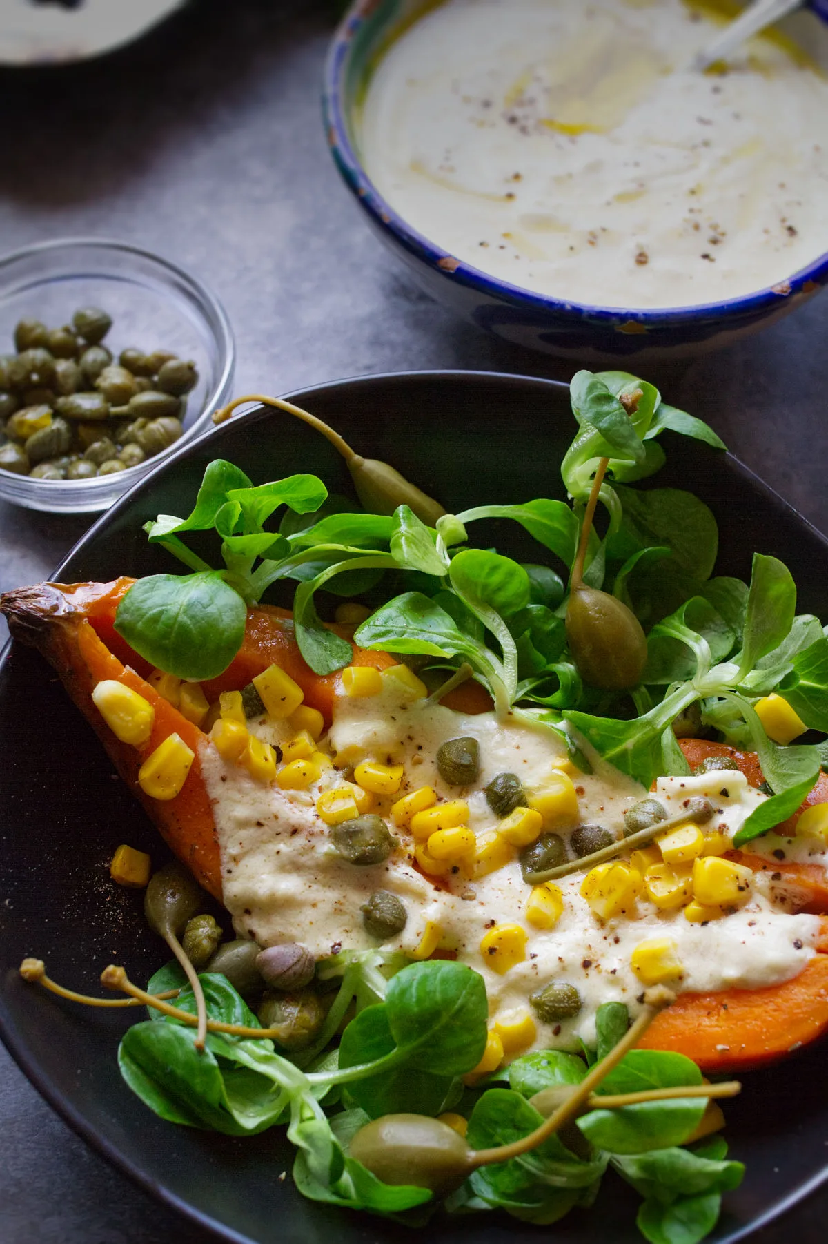 A baked sweet potato in a bowl with some salad and a dressing on top.