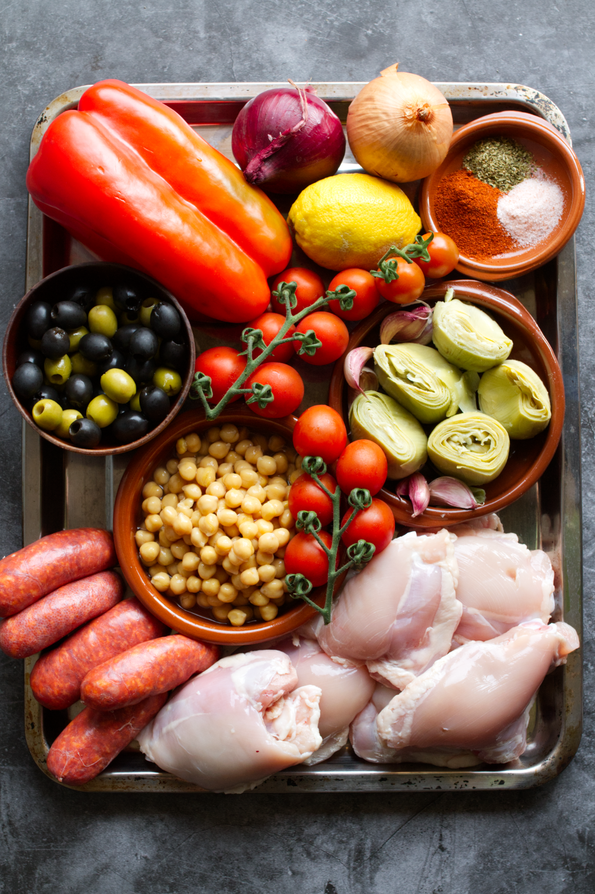 ingedients for making sheet pan chicken thighs with chorizo and roast veg sit in a sheet pan with some spices.