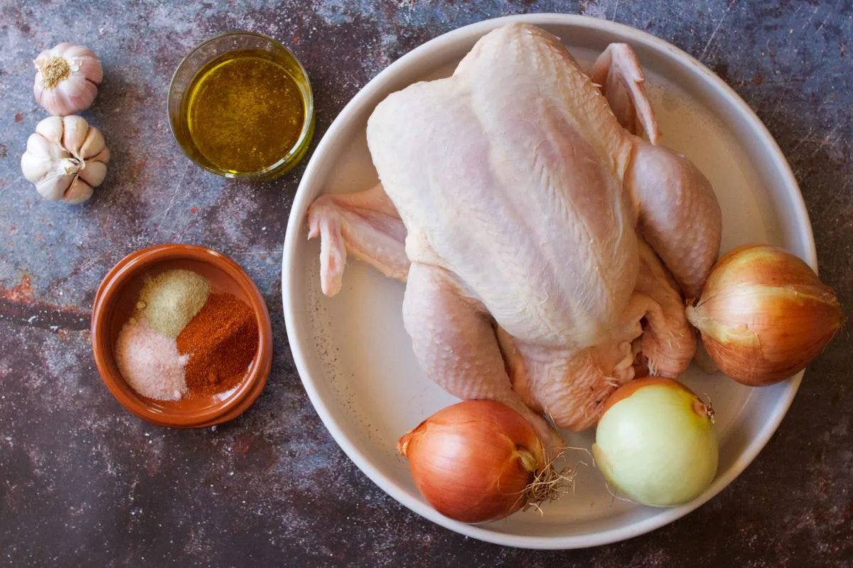 A large raw chicken with some onions, spices, and garlic.