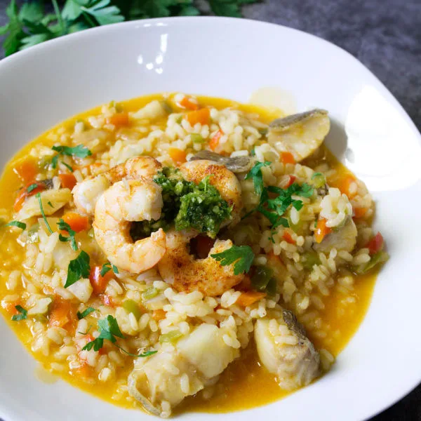 A bowl of brothy fish stew topped with some almond pesto and pan-fried shrimp.