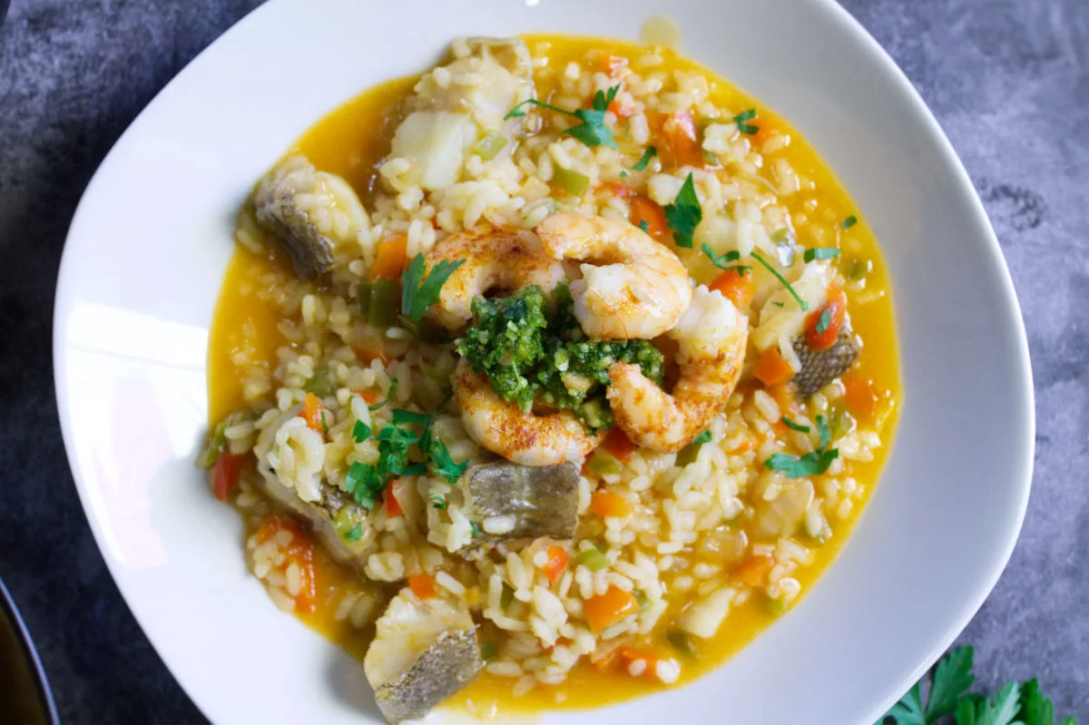 A bowl of brothy fish stew topped with some almond pesto and pan-fried shrimp.