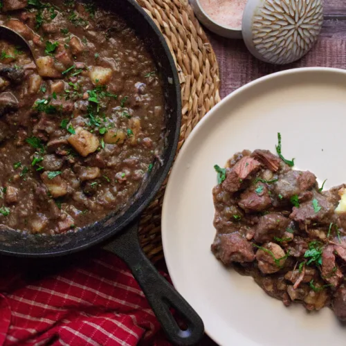 A large pot of catalan style beef stew sits beside a plate serving