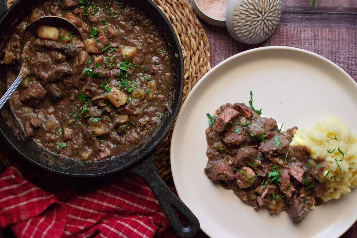 A large pot of catalan style beef stew sits beside a plate serving